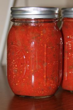 two jars filled with red sauce sitting on top of a wooden table