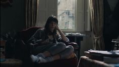 a woman sitting on top of a chair in a living room next to a window