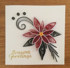 a white card with red and black paper flowers on it, which reads seasons greetings