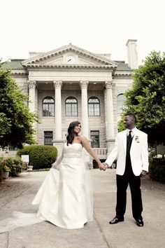 a bride and groom holding hands in front of a large building