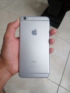 a hand holding an iphone in front of a white tile floor with a black object behind it