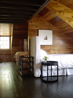 a bedroom with wood paneling and white bedding in the corner next to a small side table