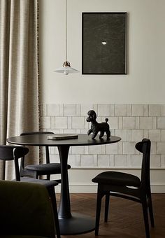 a black dog figurine sitting on top of a table next to two chairs