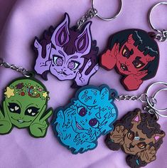 four cartoon keychains are shown on a purple cloth with an image of three different monsters