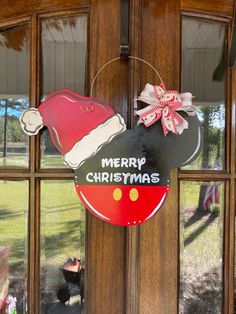 a mickey mouse christmas ornament hanging on a door with a santa hat and bow