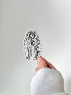 a hand holding up a sticker depicting the virgin mary