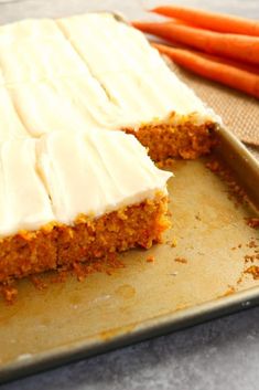 carrot cake with cream cheese frosting on a baking sheet next to carrots and a spatula