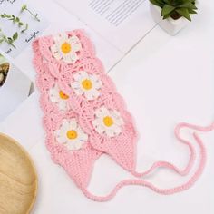 a pink crocheted bag with white flowers on it and a wooden bowl next to it