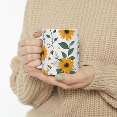 a woman holding a coffee mug with sunflowers on the front and sides in her hands