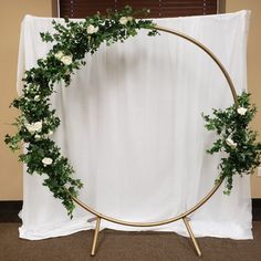 a white rose and greenery wreath on a gold metal stand in front of a white backdrop