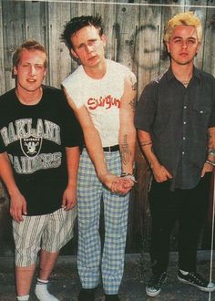 three men standing next to each other in front of a wooden fence