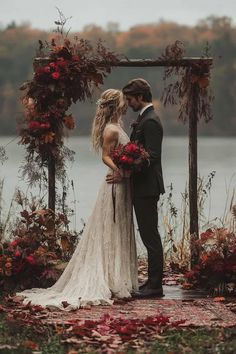 a bride and groom are standing in front of an arch with red flowers on it