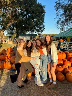 four girls standing in front of a pile of pumpkins at a pumpkin patch with their arms around each other