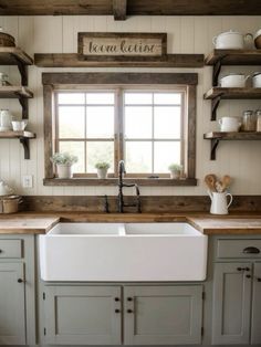 a white kitchen sink sitting under a window next to wooden shelves and open shelving