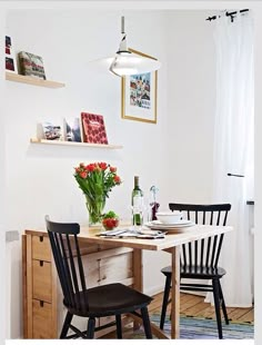 a small dining table with two chairs and a vase of flowers on the top shelf