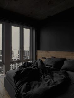 an unmade bed with black sheets and pillows in front of large windows overlooking the city