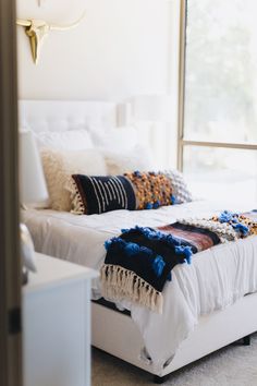 a white bed sitting in a bedroom next to a window with lots of pillows on top of it