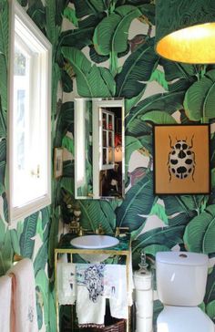 a bathroom decorated in green and white with palm leaves on the wall behind the toilet