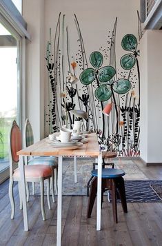 a dining room table with plates and cups on it next to a wall painted with plants