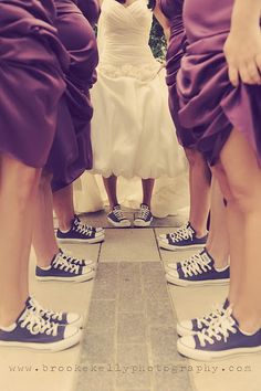 three bridesmaids in purple dresses and converse shoes with their feet up on the ground