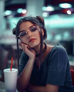 a woman wearing glasses sitting at a table with a drink in front of her face