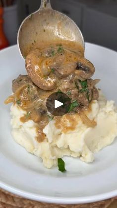 a white plate topped with mashed potatoes covered in mushroom gravy and a spoon