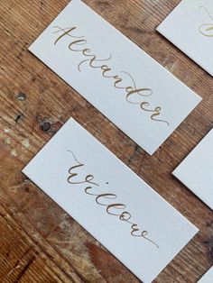 three white cards with gold lettering on them sitting on a wooden table next to each other