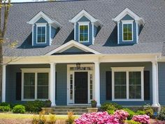 a blue house with white trim and black shutters on the front door is surrounded by pink flowers