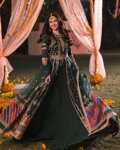 a woman in a green and gold dress standing under an arch with flowers on it