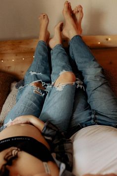 a woman laying on top of a bed with her legs crossed and wearing ripped jeans