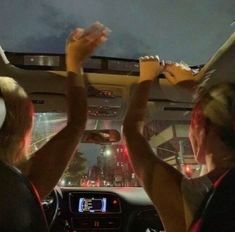 two women are sitting in the back seat of a car and one is holding her hand up