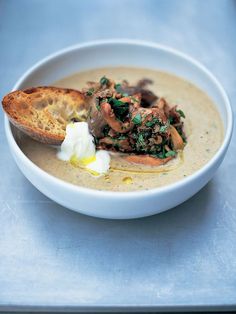 a white bowl filled with soup and bread on top of a blue tablecloth next to a piece of bread