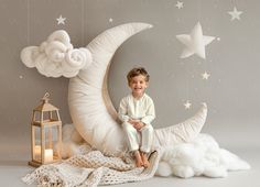 a little boy sitting on the moon in front of a wall mural with stars and clouds