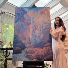 a woman standing in front of a painting holding up a piece of art with her hands