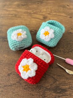 three crocheted baby shoes with flower appliques on them, one is red and the other is blue