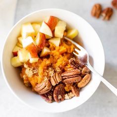 a bowl filled with fruit and nuts on top of a white countertop next to a fork