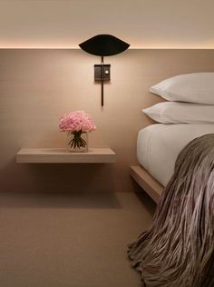 a vase with pink flowers sitting on a table next to a wall light and bed