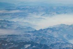 the view from an airplane looking down on mountains and clouds in the sky with blue hues