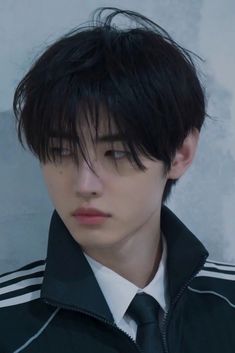 a young man with black hair wearing a jacket and tie, looking at the camera