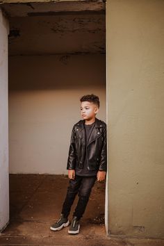 a young boy standing in an open doorway wearing black leather jacket and jeans, looking at the camera