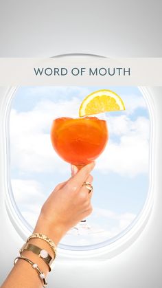 a person holding up a drink with the words word of mouth in front of an airplane window