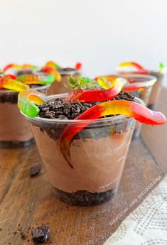 three cups filled with chocolate pudding and colorful toppings on top of a wooden table