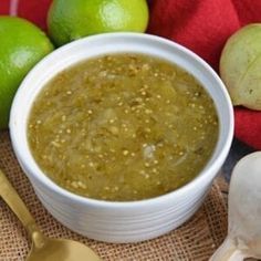 a white bowl filled with green liquid next to limes and garlic on a table