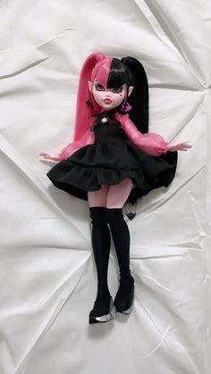 a doll with pink hair and black dress laying on a white sheet in the shape of a heart