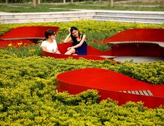 two women are sitting in the middle of a garden with red curved benches and yellow flowers