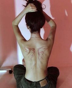 a woman sitting on the floor with her back turned to the camera and tattoos on her chest