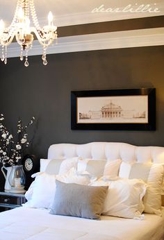 a white bed sitting under a chandelier next to a wall with pictures on it