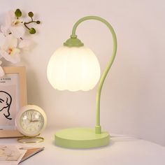 a green lamp sitting on top of a white table next to a clock and flowers