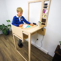 a young boy sitting at a wooden desk with a mirror on the wall behind him