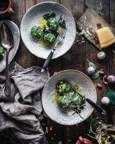 two white bowls filled with broccoli on top of a wooden table next to silverware